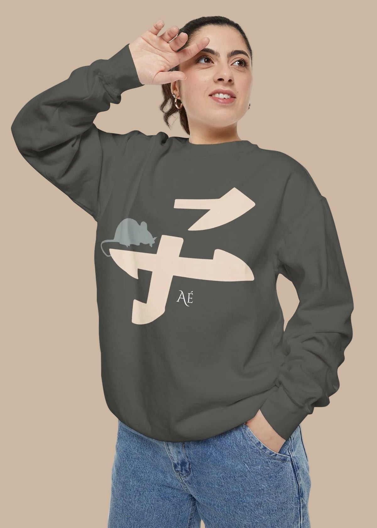 A woman wearing a dark gray crewneck sweatshirt with a graphic of a mouse riding a large beige character, paired with blue jeans, set against a plain white background.