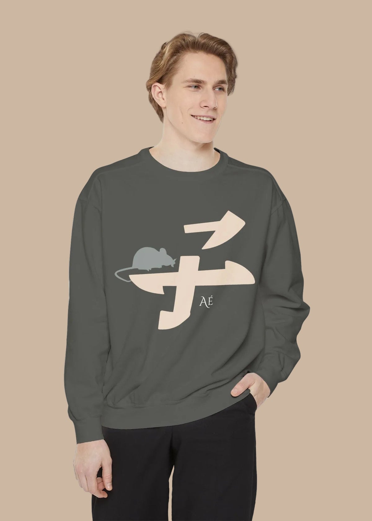 A man wearing a dark gray crewneck sweatshirt with a beige and gray graphic of a mouse inside a stylized character, paired with black pants, against a plain white background.